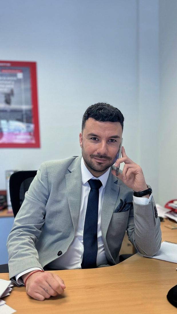 Eftim en su despacho con traje gris y corbata azul, hablando por teléfono